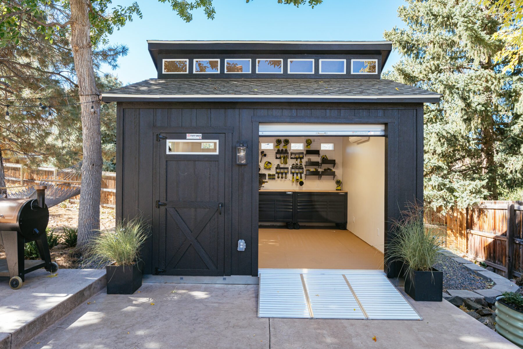 Black woodworking Tuff Shed with roll up door and pegboard.